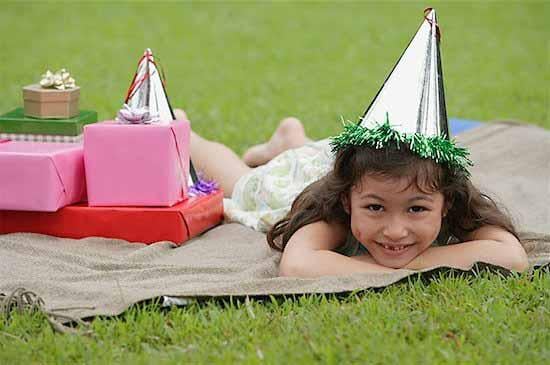 birthday girl, girl lying on picnic blanket, wearing party hat, smiling at camera