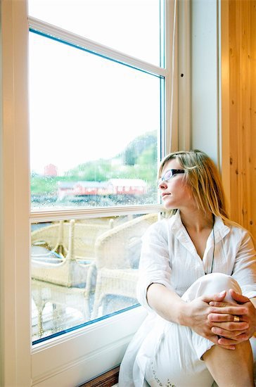blonde woman looking out window, thinking, wearing glasses