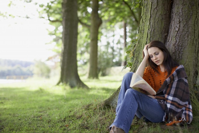 woman reading book in park against tree