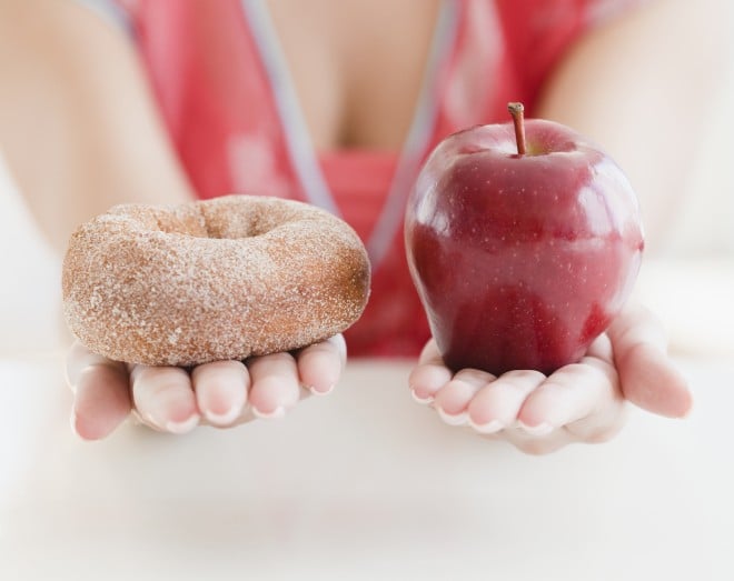 woman holding donut and apple in hands, deciding on food