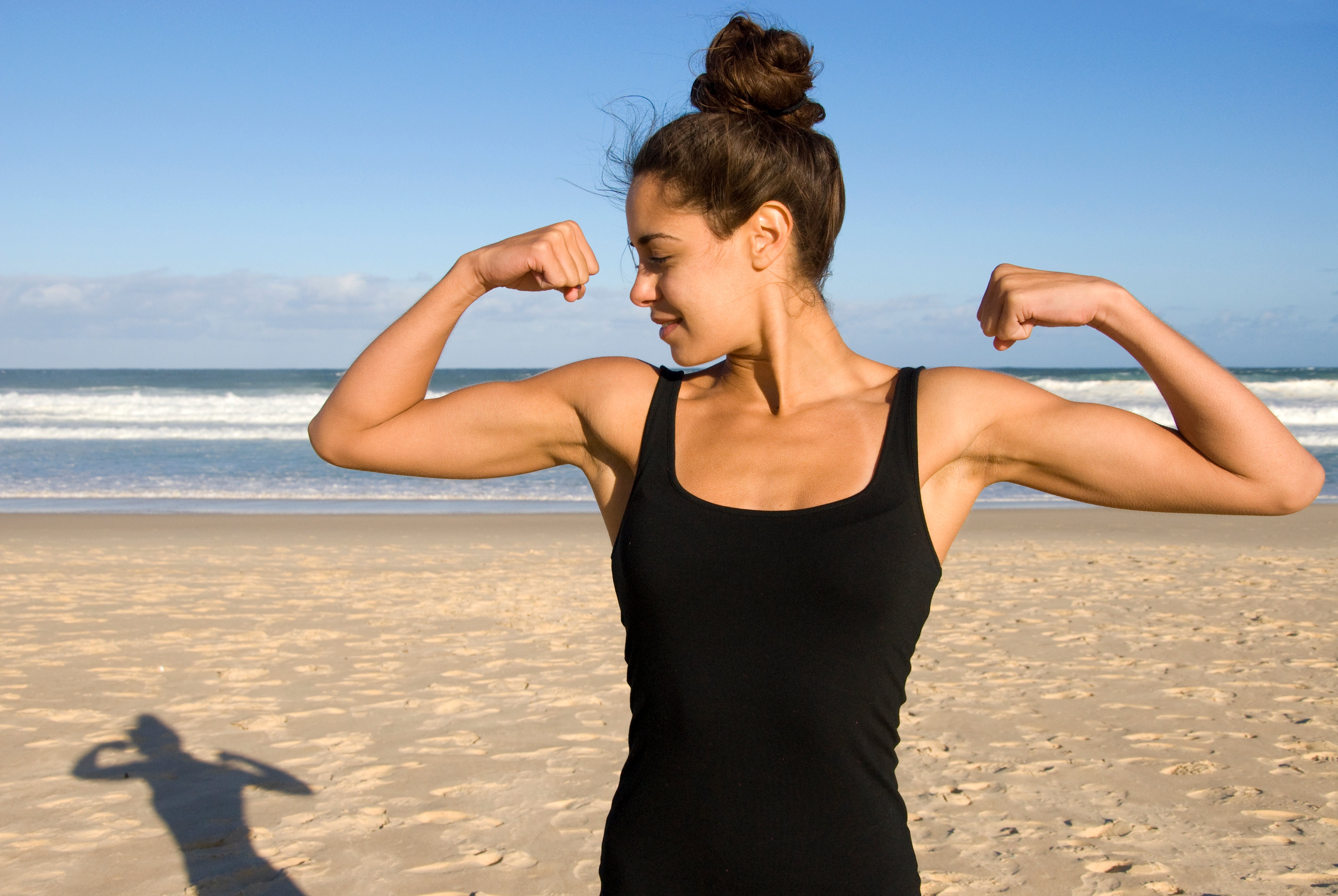 woman showing biceps standing on beach, strength, fitness