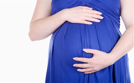 A woman in a blue dress holding her pregnant belly