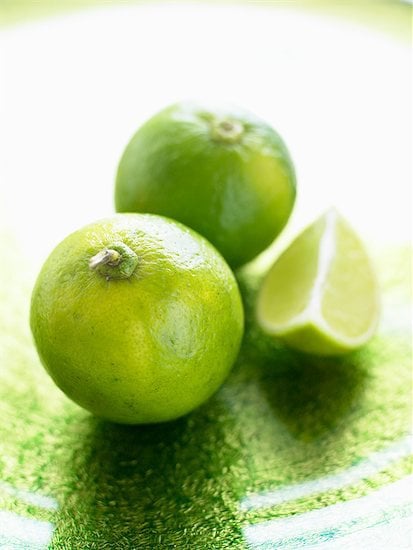 Three limes sitting on a table, one sliced