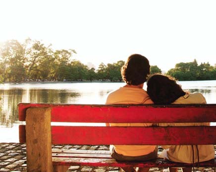Couple Sitting On Bench Overlooking Lake