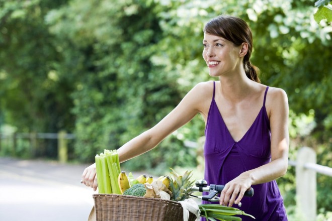 Woman walks bike with basket full of healthy foods