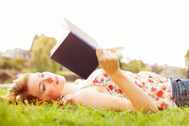 woman in floral print laying on grass reading a book
