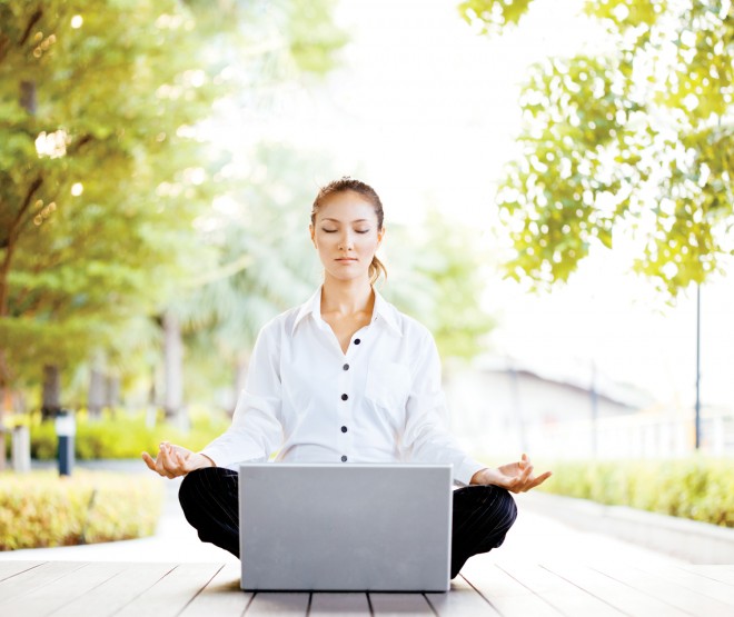 Woman meditating in front of laptop on deck, outdoors