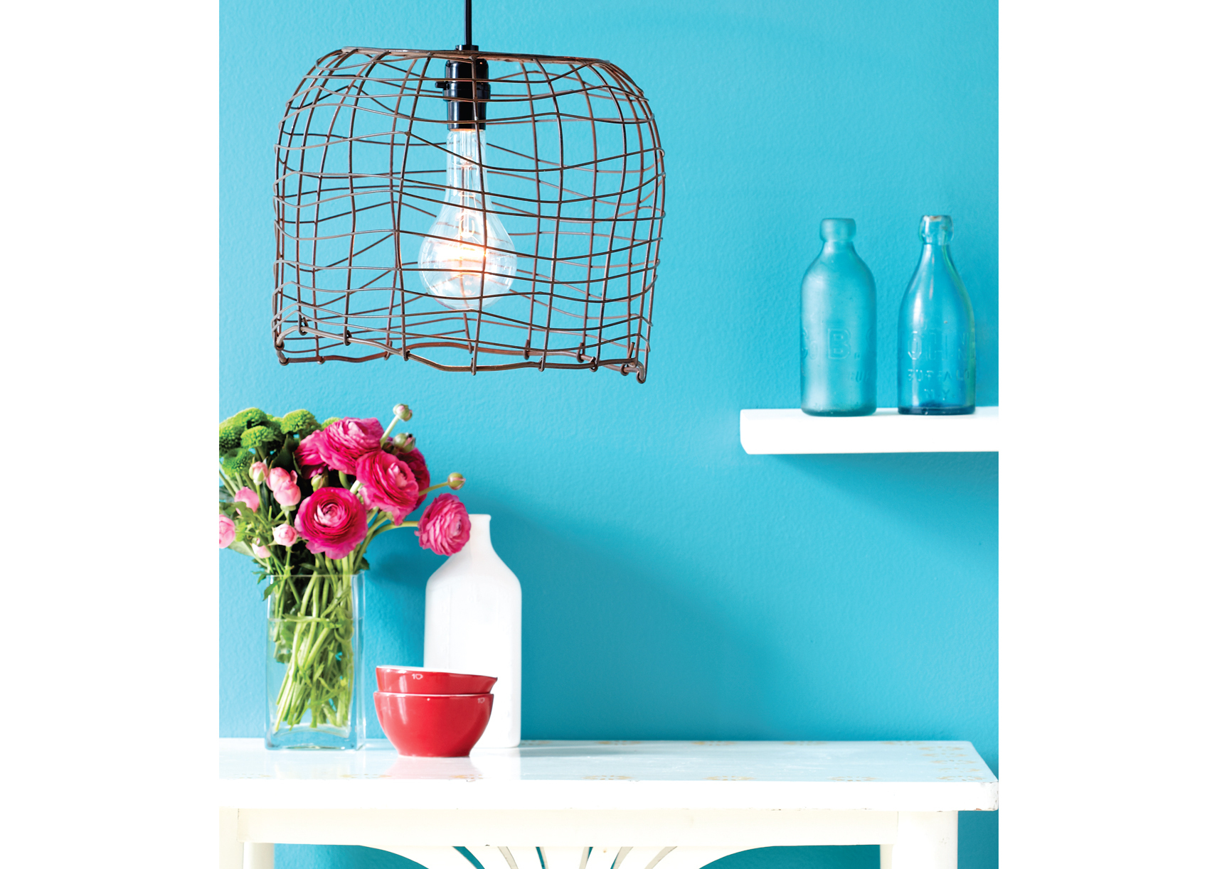 Wire basket lamp, blue wall, white shelf, white table, light bulb, flowers, bottles