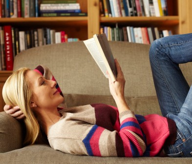blonde woman reading book on living room couch