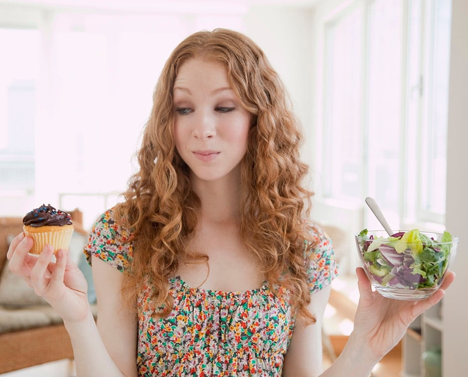 Woman debating between a cupcake and a salad