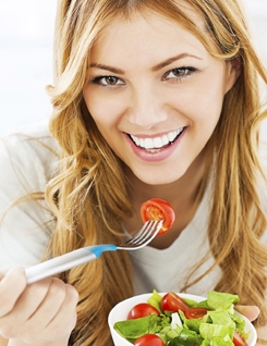 Cheerful blonde woman holding a bowl of vegetable salad and she is eating it