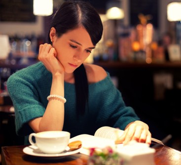 woman with black hair reading a book in coffee shop