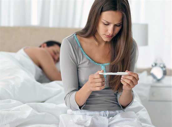 Woman holding a pregnancy test on her bed
