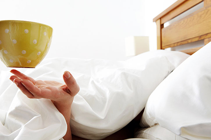 Woman being handed coffee in bed