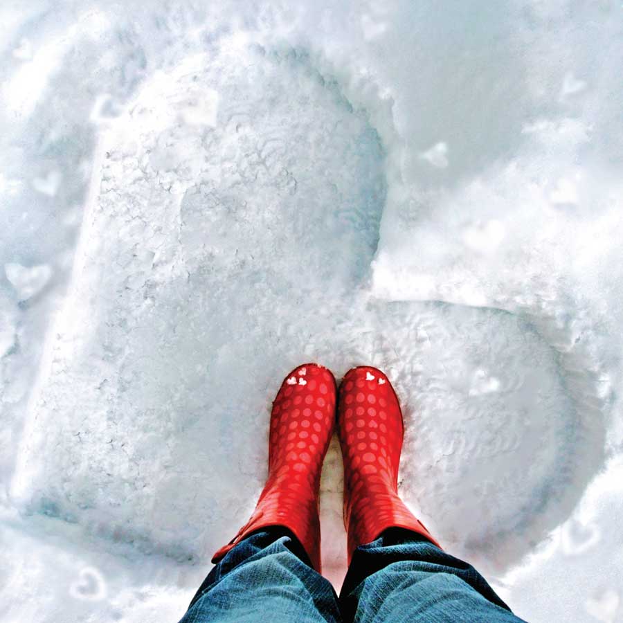 Woman standing in the snow wearing boots with a heart