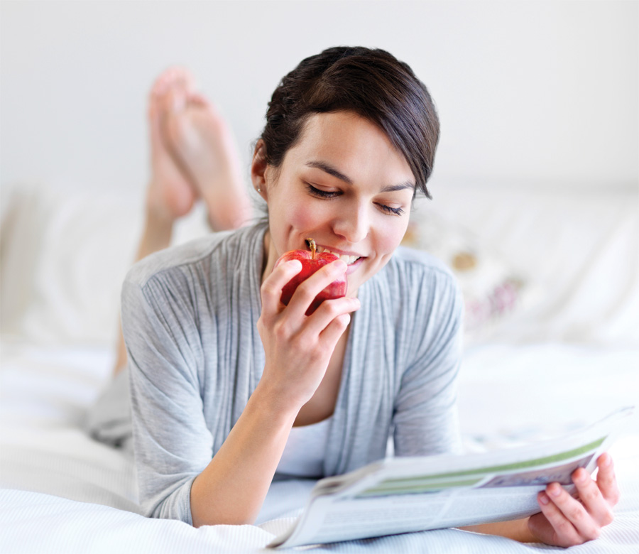 happy healthy woman eating apple in bed