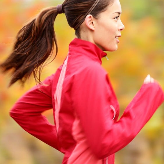 A jogger runs in the fall wearing a pink jacket
