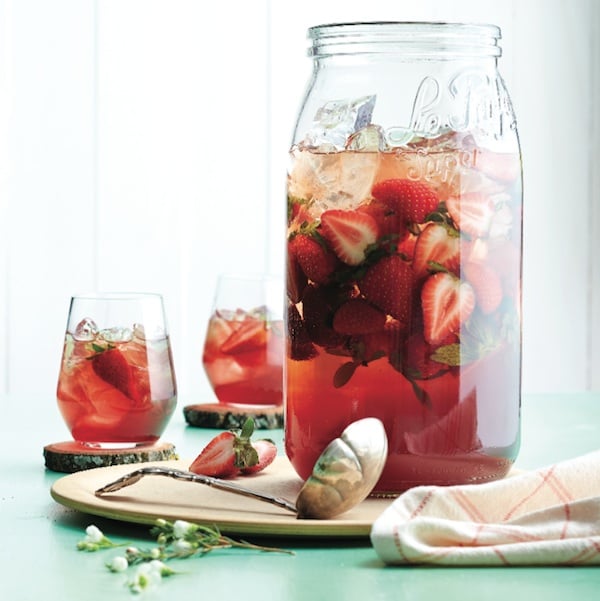Strawberry sangria in a large pitcher with a ladle ad full glasses to the side on a table.