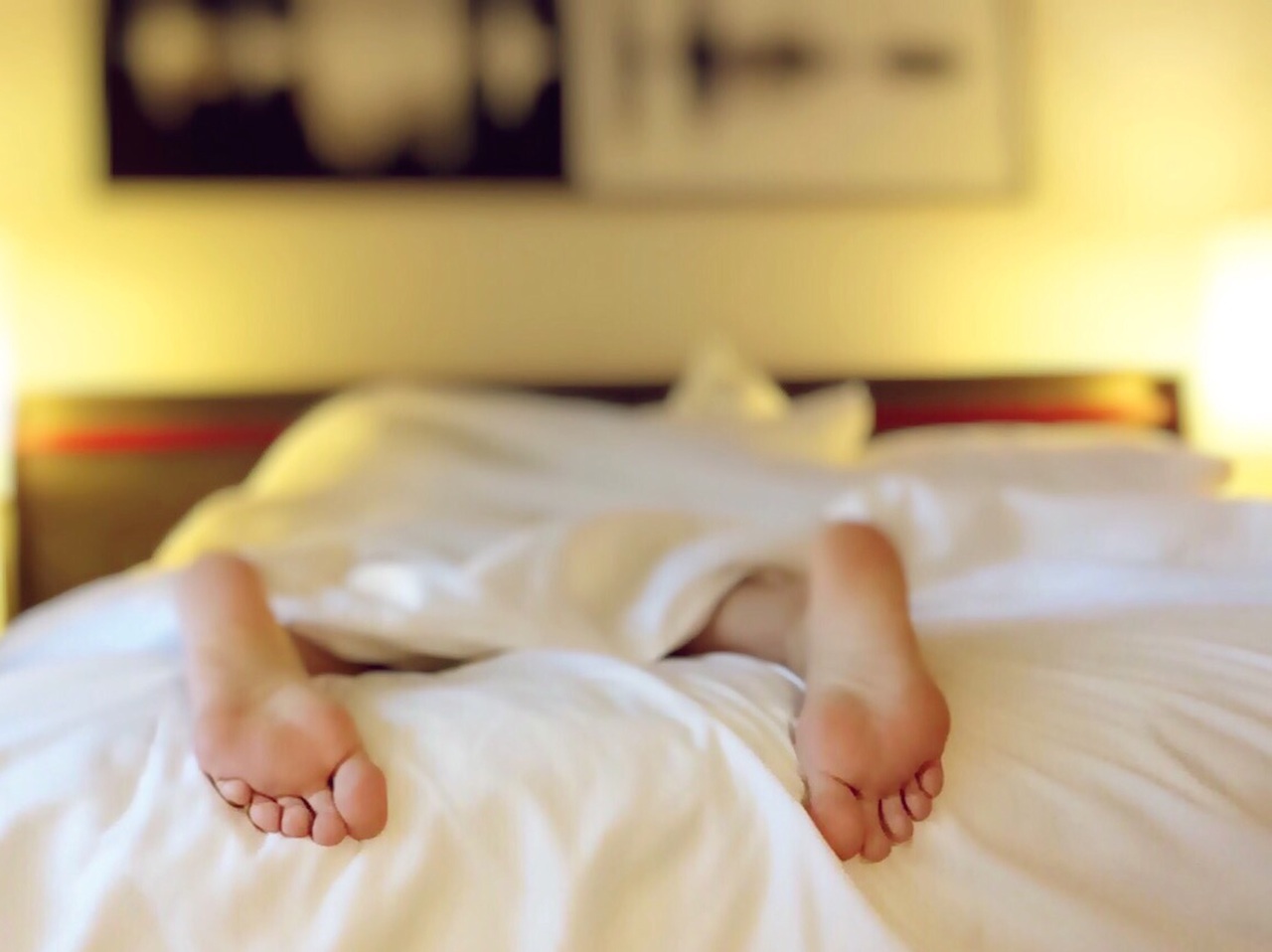 A person lies on their belly in bed, feet sticking out the end. How many hours of sleep do you really need?