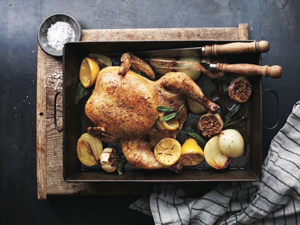 classic roast chicken on a roasting pan with lemons, onions and herbs