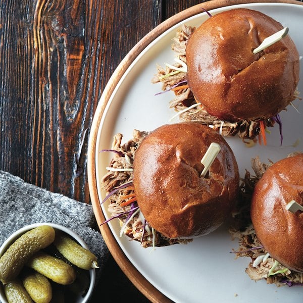 pulled pork recipe served in bun with coleslaw and pickles on the side