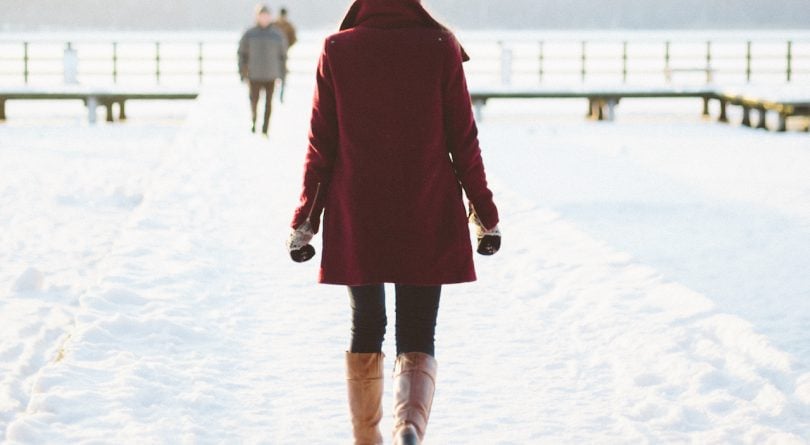 salt stains- image of a woman walking in the snow with tall brown boots and a red coat