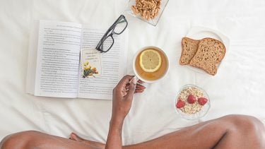 overhead flat shot of a woman sitting cross-legged in bed eating toast granola and tea