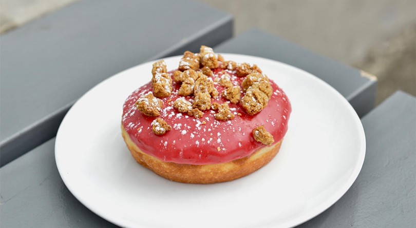 Red frosted doughnut sits on a white plate, from Lucky's Doughnuts in Vancouver. best doughnut shops canada