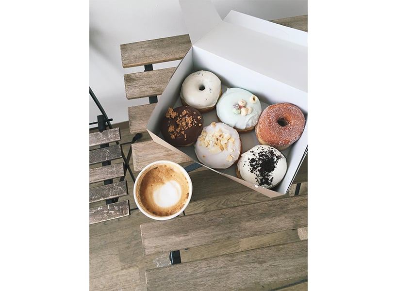 A box of six assorted doughnuts and a latte from Suzy Q in Ottawa sit on a wooden table.