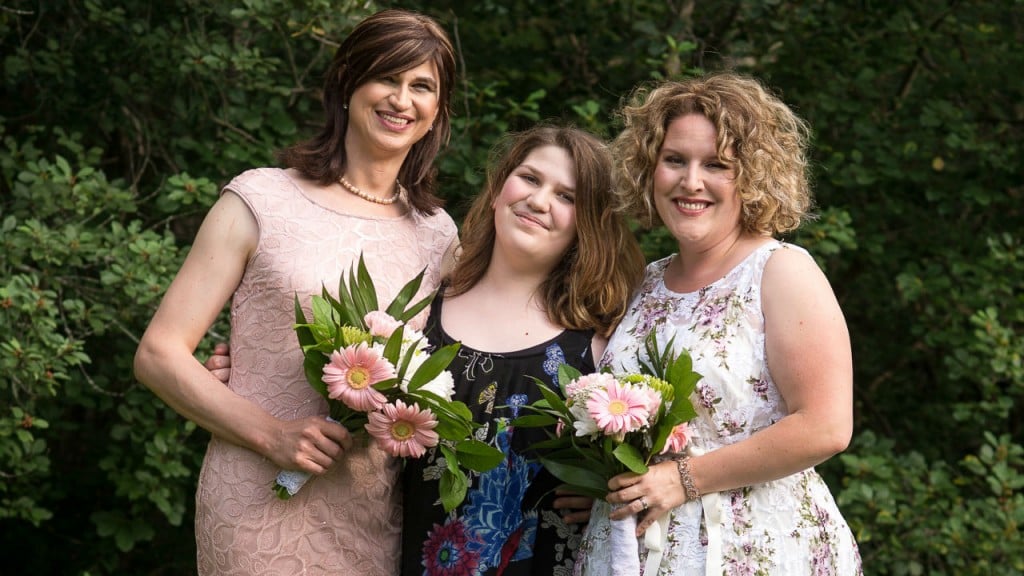 trans daughter-Zoe and Amanda pose on their wedding day with one of their children.