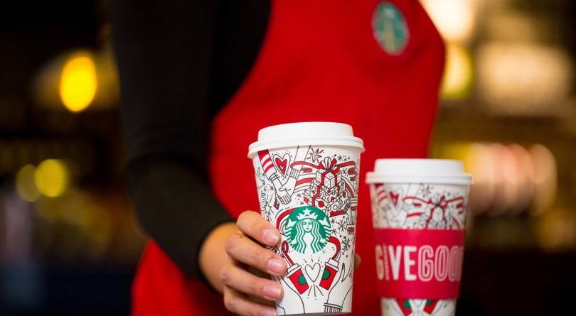 Barista in a red apron placing Satrbucks holiday drink on counter next to another cup