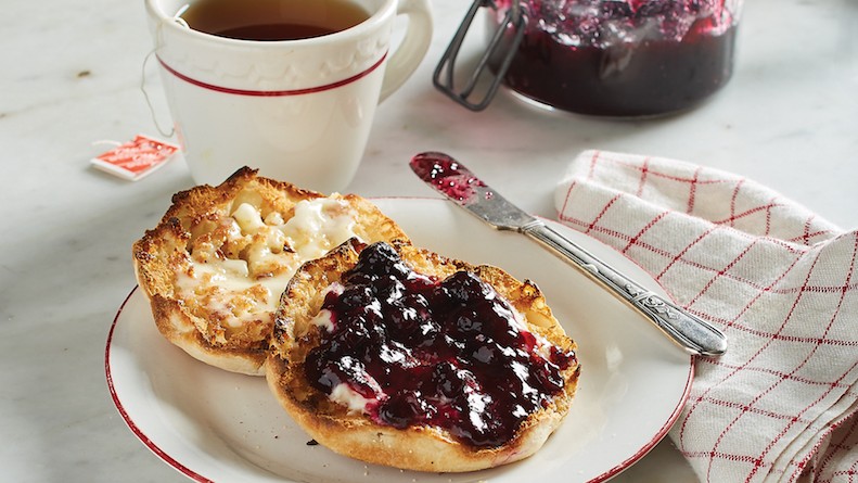 English muffin on plate covered in blueberry jam
