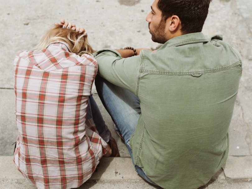 fear of breaking up-a man and woman sit huddled on a sidewalk, heads down, looking mad