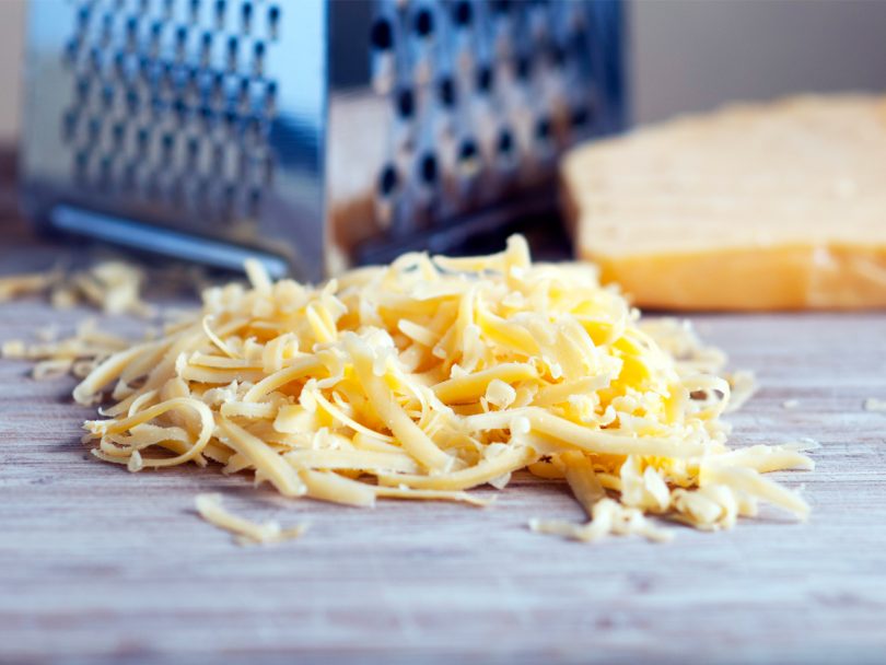Pile of shredded cheese in front of box grater