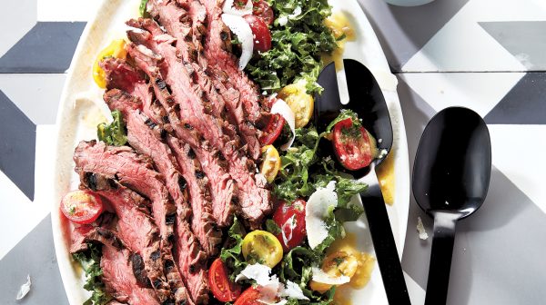 Grilled flank steak caesar salad with serving spoons and a side of dressing