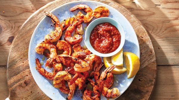 grilled piri piri shrimp with cocktail sauce on a blue plate over a round wooden tray