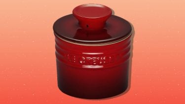 Image of a red le creuset butter crock on a gradient orange background.