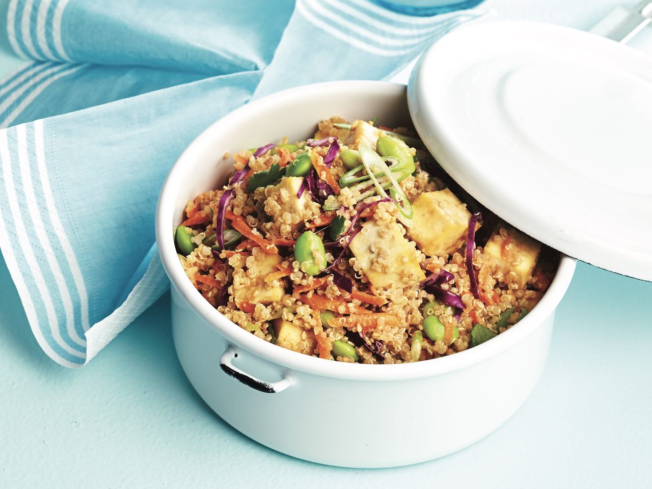 Thai quinoa and tofu salad in a white bowl with a lid angled over it to the side
