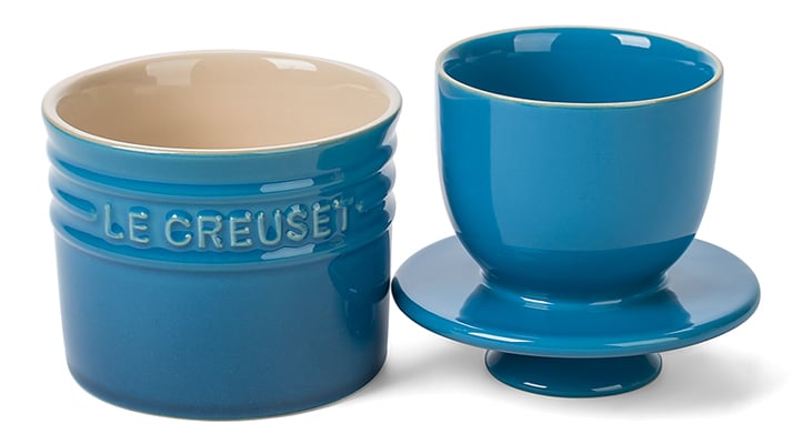 Image of a blue Le Creuset butter crock on a white background. The two parts are shown side by side, with the base on the right and the lid with the butter-holder cup on the right. 