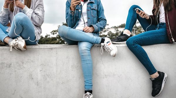 teenage girl on social media feature image shows girls sitting on a cement wall while using their phones