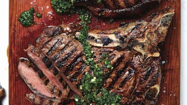Two steak on wooden board covered in herb sauce.