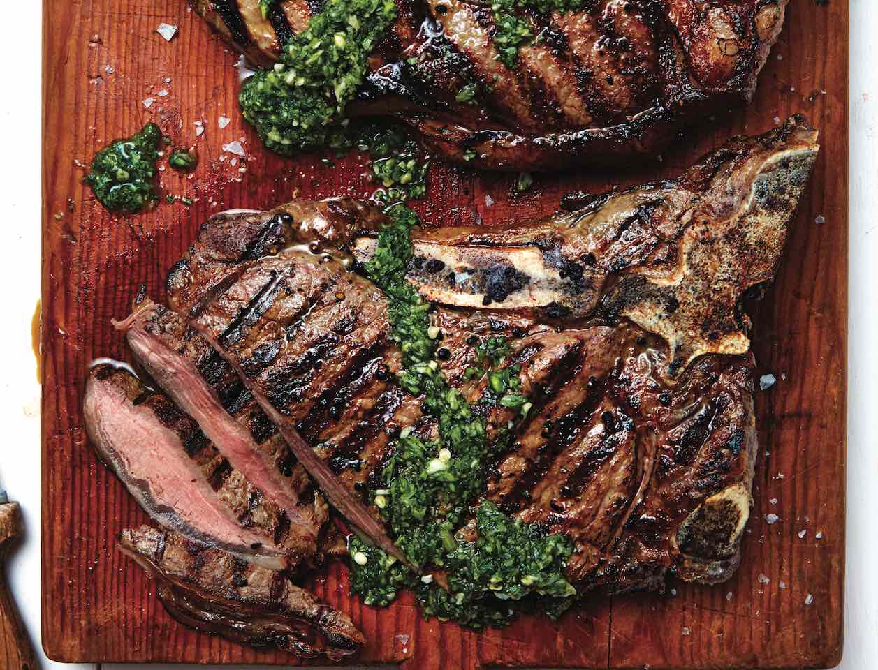 Two steak on wooden board covered in herb sauce.