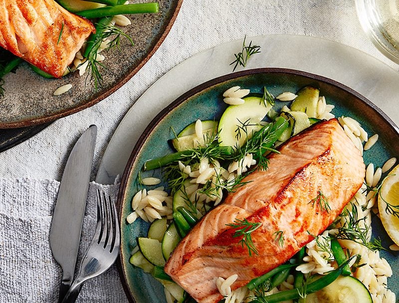 Salmon fillet on bed of orzo salad served on grey plates