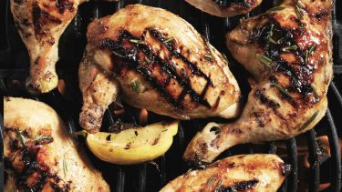 Chicken legs and lemon wedges on grill