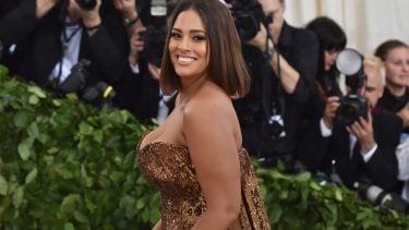 celebrities on body hair: Ashley Graham in brown sequinned dress while photographers snap photos from behind a leafy barrier.