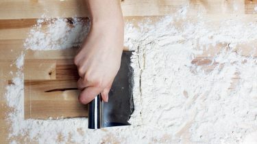 Bench scraper with flour on wooden board