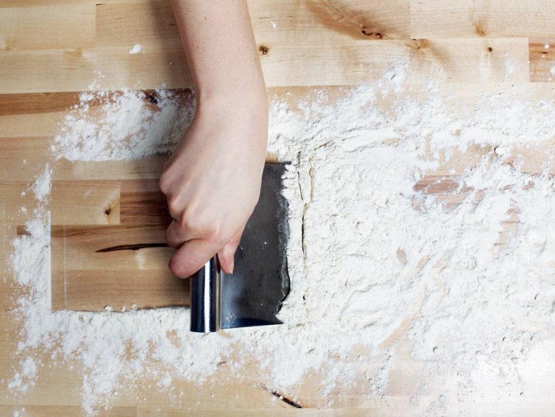 Bench scraper with flour on wooden board