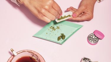 how to smoke weed - a pair of hands are rolling a joint on a pink table