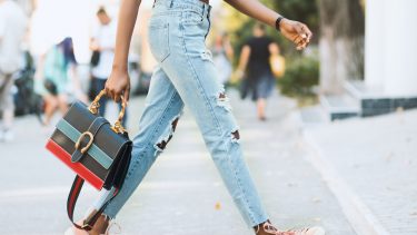 woman wearing jeans and pink sneakers carrying a handbag walking down the street