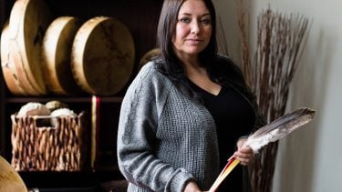 Human Trafficking - woman with short brown hair wearing grey sweater holds a large feather and stands by traditional aboriginal drums